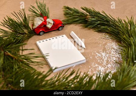 Spruce wreath with a red car with a bag of gifts, on the table framing white notebook and pencil crayon near snow chips. Stock Photo