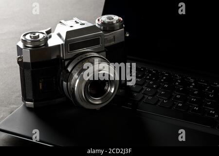 Retro analog SLR camera on laptop keyboard on black desk in office, digital photography or image processing concept, selective focus Stock Photo