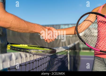 Tennis players shaking hands at court net at end of fun game. Man and woman playing recreational tennis handshaking with tennis racquets. Stock Photo