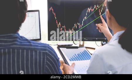 broker showing some ascending to his colleague planning and analyzing graph stock market trading with stock chart data on multiple computer screens Stock Photo