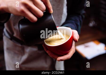 Barista pours fresh milk into a cup of coffee. latte art Stock Photo