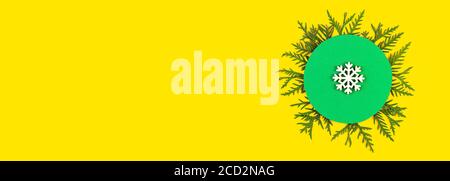 Christmas banner with coniferous tree branches and snowflake on yellow paper background. Round frame of Christmas tree branches and decorations with s Stock Photo