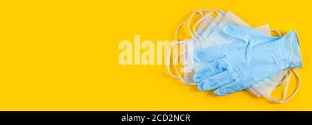 Long wide banner. Pair of latex medical gloves and surgical ear-loop mask on yellow background. Hygiene protection Coronavirus Covid 19. hygiene items Stock Photo