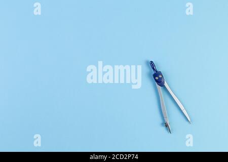 School compass for drawing circles in geometry. Isolated on blue paper background. back to school concept with stationery. With copy space, template f Stock Photo