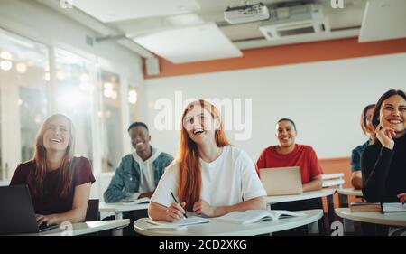 Group of teenage students smiling during the lecture in classroom. University students laughing in classroom. Stock Photo