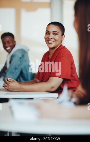 Smiling female student sitting at desk in high school classroom.  Girl with short hair smiling in university classroom. Stock Photo