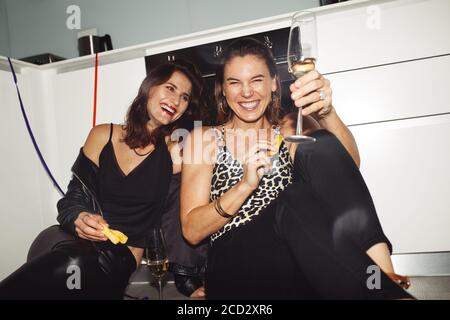 Happy women friends having fun at home enjoying wine. Two cheerful women having a party sitting on floor at home. Stock Photo
