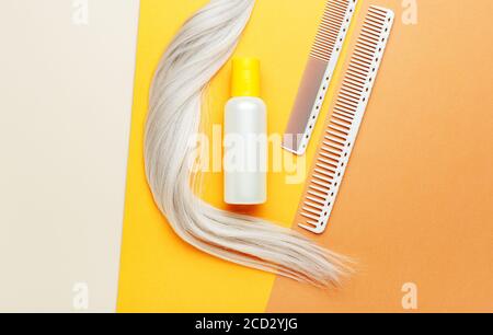 Shampoo orange bottle with lock curl of blonde hair and combs. Hairdresser tools, hair salon equipment for hairdressing in beauty salon, barber shop Stock Photo