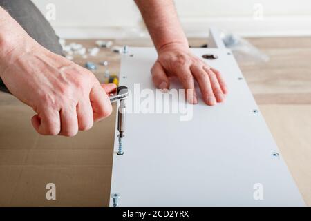 Furniture assembly. Male hands master collects furniture using screwdriver tools, instrument at home. Moving, home improvement, furniture repair and Stock Photo