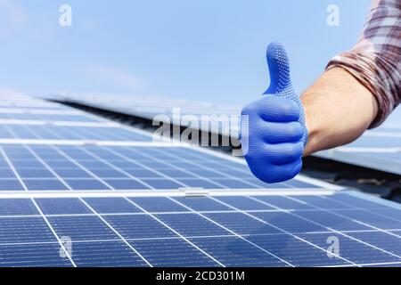 Male worker showing thumbs up, positive gesture against solar panel, solar station. Like to alternative energy sun energy power. Man installing solar Stock Photo