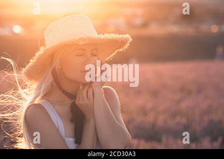 Young beautiful blonde woman 24-26 year old wearing straw hat with laces posing with eyes closed in meadow over nature background. Summer season.