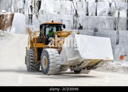 Heavy duty front end loader moving a large block of white Carrara marble in an open cast mine or quarry in Tuscany, Italy Stock Photo