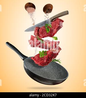 Flying raw steaks, with ingredients for cooking, from pan. wooden bowls with spices. Concept of food preparation. Separated on brown background. Extra Stock Photo