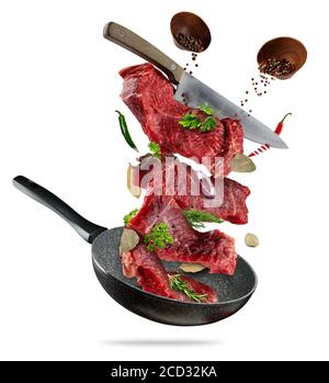Flying raw steaks, with ingredients for cooking, from pan. wooden bowls with spices. Concept of food preparation. Isolated on white background. Extra Stock Photo