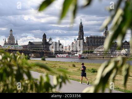 Dresden, Germany. 26th Aug, 2020. A jogger runs along the Elbe cycle path in front of the old town scenery with the Frauenkirche (l-r), the Ständehaus, the town hall, the Kreuzkirche, the Georgentor, the Hofkirche, the Hausmannsturm and the Residenzschloss while clouds pass over it. Credit: Robert Michael/dpa-Zentralbild/dpa/Alamy Live News Stock Photo