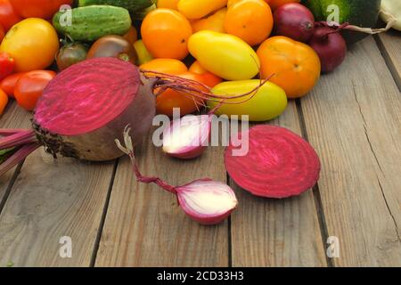 Sliced ​​beets and onions lie on a wooden board against a background of different bright vegetables. Harvest and cooking concept. Stock Photo