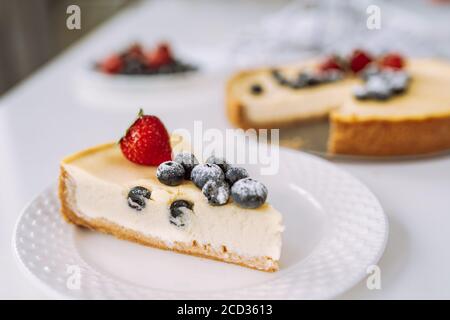Piece of homemade cheesecake with fresh strawberry and blackberry on a white plate on a table. Stock Photo