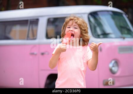 Kids with ice cream. Child eating ice cream in a pink wall background. Small boy holds ice-cream and looks happy and surprised. Stock Photo