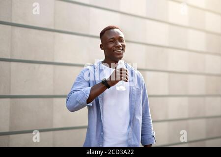 Joyful black guy drinking clear water from bottle on city street Stock Photo