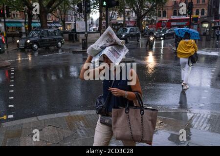During an early evening downpour in Sloane Square, a lady covers her head with the latest edition of the Evening Standard newspaper, on 24th August 2020, in London, England. Stock Photo