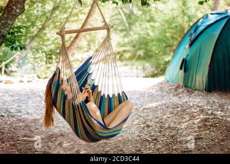 A young woman relaxing in a hammock. Girl resting in a hammock in the woods. Camping and healthy lifestyle in the forest. Stock Photo