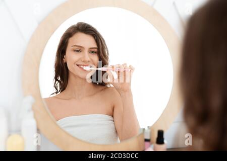 Happy young woman brushing teeth in bathroom Stock Photo