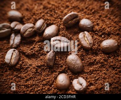 Several roasted aromatic natural coffee beans lie in a pile of ground coffee, illuminated by light. The transformation of beans into ground coffee. An Stock Photo