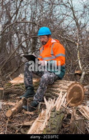 Forestry technician writing notes on clipboard notepad paper in forest during logging deforestation process Stock Photo