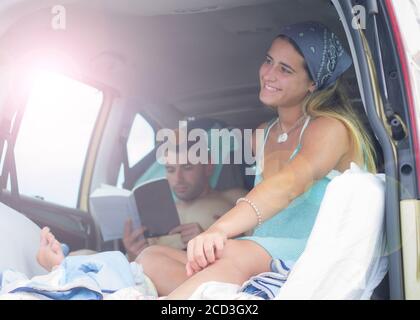 Young couple enjoy camping holidays, lying in a minivan. Reading and serenity Stock Photo