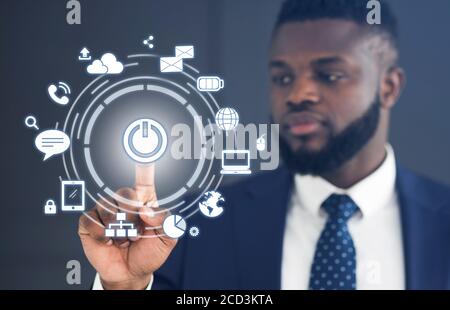 IoT. Black businessman pressing start button on virtual screen with communication icons Stock Photo
