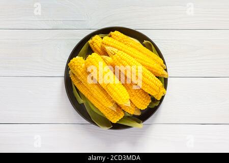 Delicious juicy sweet boiled corn in a plate on a white wooden background, cooked corn cobs Stock Photo