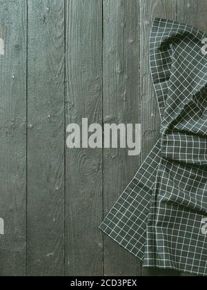 Dark wooden table with balck and white dark linen kitchen towel or textile napkin flat lay. Dark tablecloth on brown gray wood tabletop. Copy space for text. Can use as mock up for design. Vertical. Stock Photo