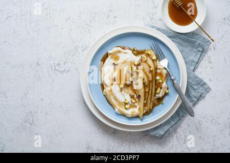 Ricotta with pears, pistachios and honey or maple syrup on blue plate on white table. Stock Photo