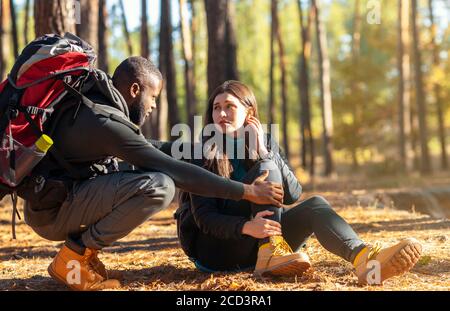 African guy comforting his girlfriend hurt her ancle while camping Stock Photo