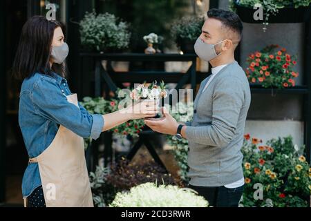 Sale of plants in flower shop. Woman in apron gives little bouquet to client