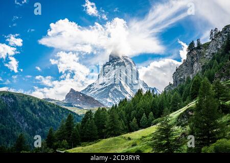 Scenic view of the Matterhorn mountain summit with snow clouds blue sky and green nature during summer in Zermatt Switzerland