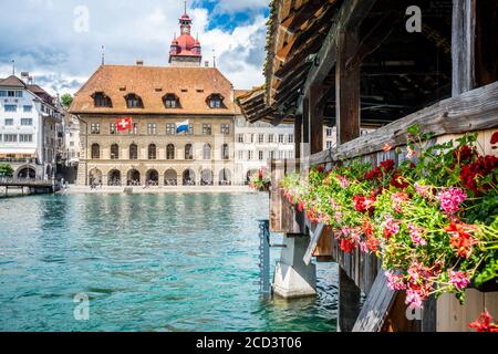 Flowers in window boxes along Chapel bridge and Swiss flag and Lucerne city hall building in background in Lucerne Switzerland Stock Photo