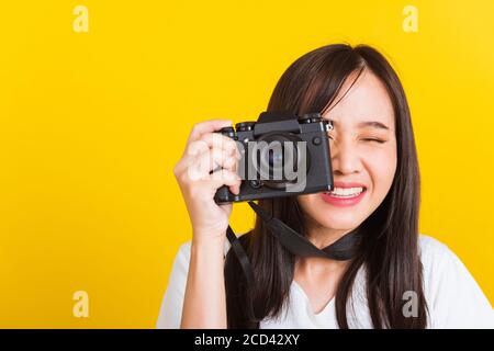 Portrait of happy Asian beautiful young woman photographer smile take picture and looking viewfinder on retro digital mirrorless photo camera ready to Stock Photo