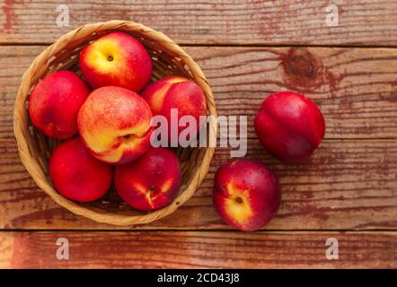 Nectarine. Ripe juicy organic nectarines (peaches) in a wicker basket. Whole fruit on a wooden table. Selective focus, top view, copy space Stock Photo