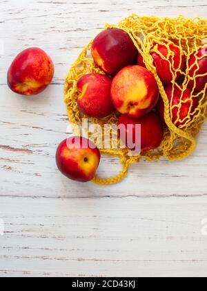 Nectarine. Ripe juicy organic nectarines (peaches) in a reusable mesh cotton shopping bag on a wooden table. plastic free zero waste concept. Selectiv Stock Photo