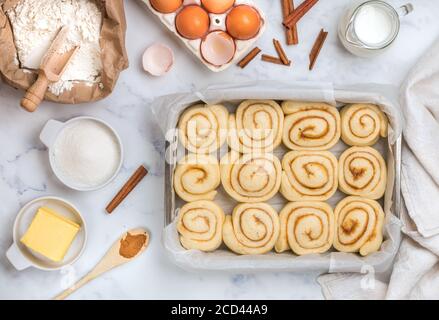 Cinnamon rolls or cinnabon handmade raw dough preparation with spices and sugar filling in a baking dish. Sweet Homemade Pastry. Ingredients on a marb Stock Photo