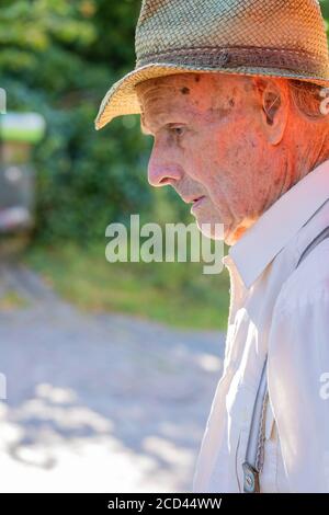 Portrait of very old farmer with straw hat thinking about life in front of a red tractor. Real retro, Closeup. Stock Photo