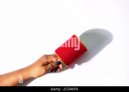Woman's hand with beautiful manicure holds red mock-up tin can on a light grey background with shadows, copy space. Top view. Stock Photo