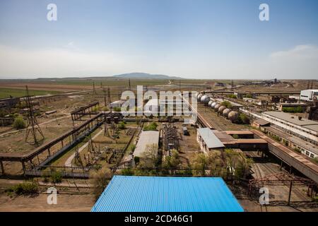 Old outdated soviet metallurgy plant. Factory buildings, rusted gas tanks, pipelines on the blue sky and mountains background. Taraz city. Stock Photo