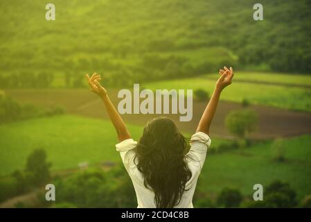 Happy celebrating winning success woman at sunset or sunrise standing elated with arms raised up above her head in celebration of having reached mount Stock Photo
