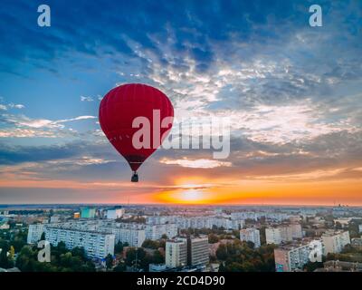 Red hot air balloon flying over small european city at summer sunrise, Kiev region, Ukraine Stock Photo