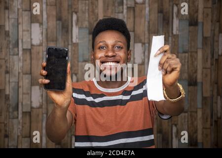 Young African male feeling excited while holding his smartphone and a paper slip Stock Photo