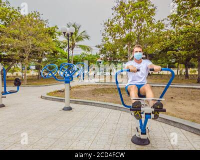 Man doing physical exercises, push ups, strength exercises, leans in empty outdoor public city park metal gym wearing mask alone for Covid19 Stock Photo