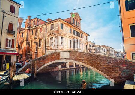Stone brick bridge Ponte Caneva across Vena water canal with moored boats and old building in historical centre of Chioggia town, blue sky background in summer day, Veneto Region, Northern Italy Stock Photo