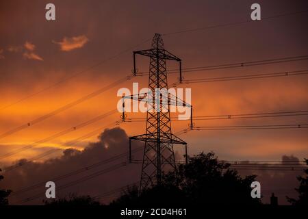 Electricity pylons feeding the local area in West Wales on a evening which the sunsets a deep orange amongst the clouds. Stock Photo